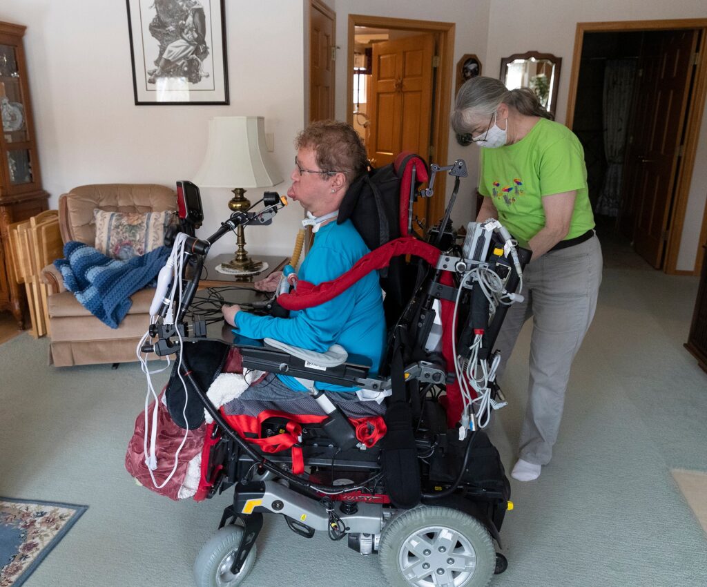 Private duty nurse Julie DuBois plugs a portable ventilator into an outlet for Timothy Carey at his home Saturday, March 19, 2022 in Grand Chute, Wis. He controls his wheelchair using his tongue. Voting in person is extremely difficult for Carey because he has advanced Duchenne muscular dystrophy and in unable to move his body. Photography by Mark Hoffman. Used with permission from the Milwaukee Journal Sentinel.