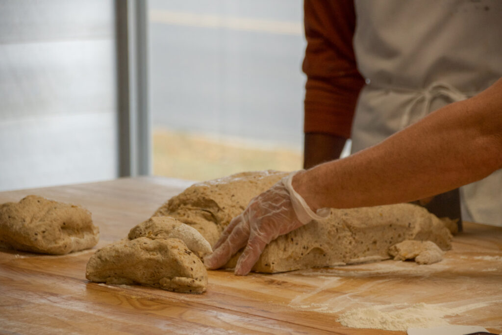 Baker handling bread dough on a cutting board.